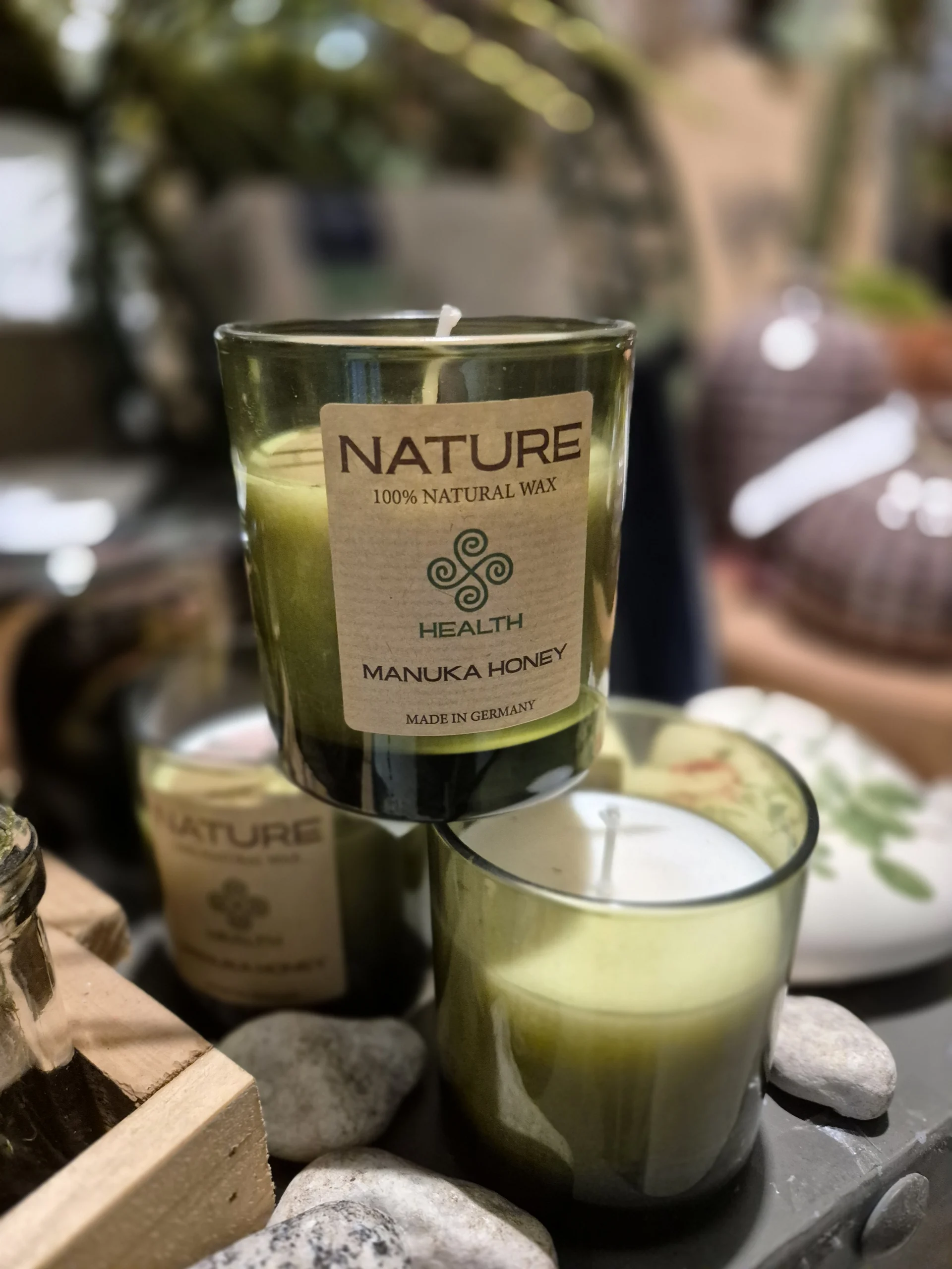 Grüne Duftkerze im Glas mit „Nature“-Label, dekorativ arrangiert zwischen Pflanzen und Keramik.